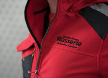 schwarzer Logo-Stick auf roter Arbeitsbekleidung; Detailaufnahme